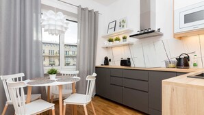 A modern kitchen with a round dining table, white chairs, grey cabinets, and a window with grey curtains. - Jerozolimskie Central View Apartment (Warsaw)