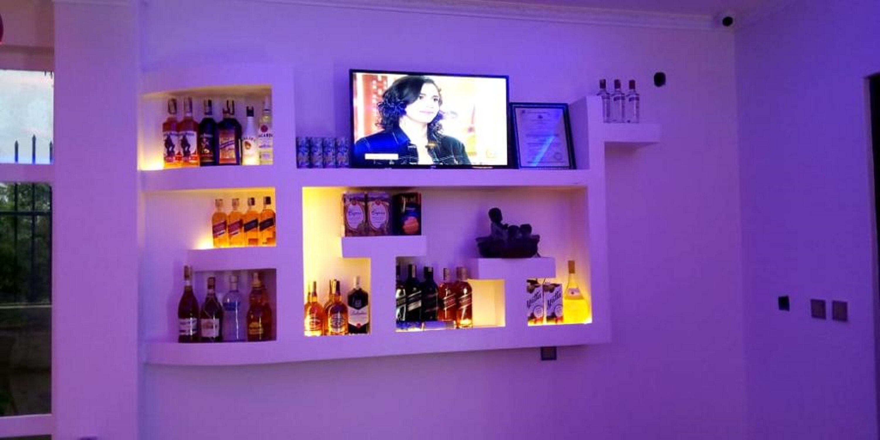 Zona de bar con estantes llenos de botellas de licores y una pantalla de televisión.