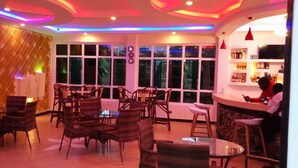 Un restaurante con varias mesas y sillas, una zona de bar y ventanas amplias con vistas al exterior.