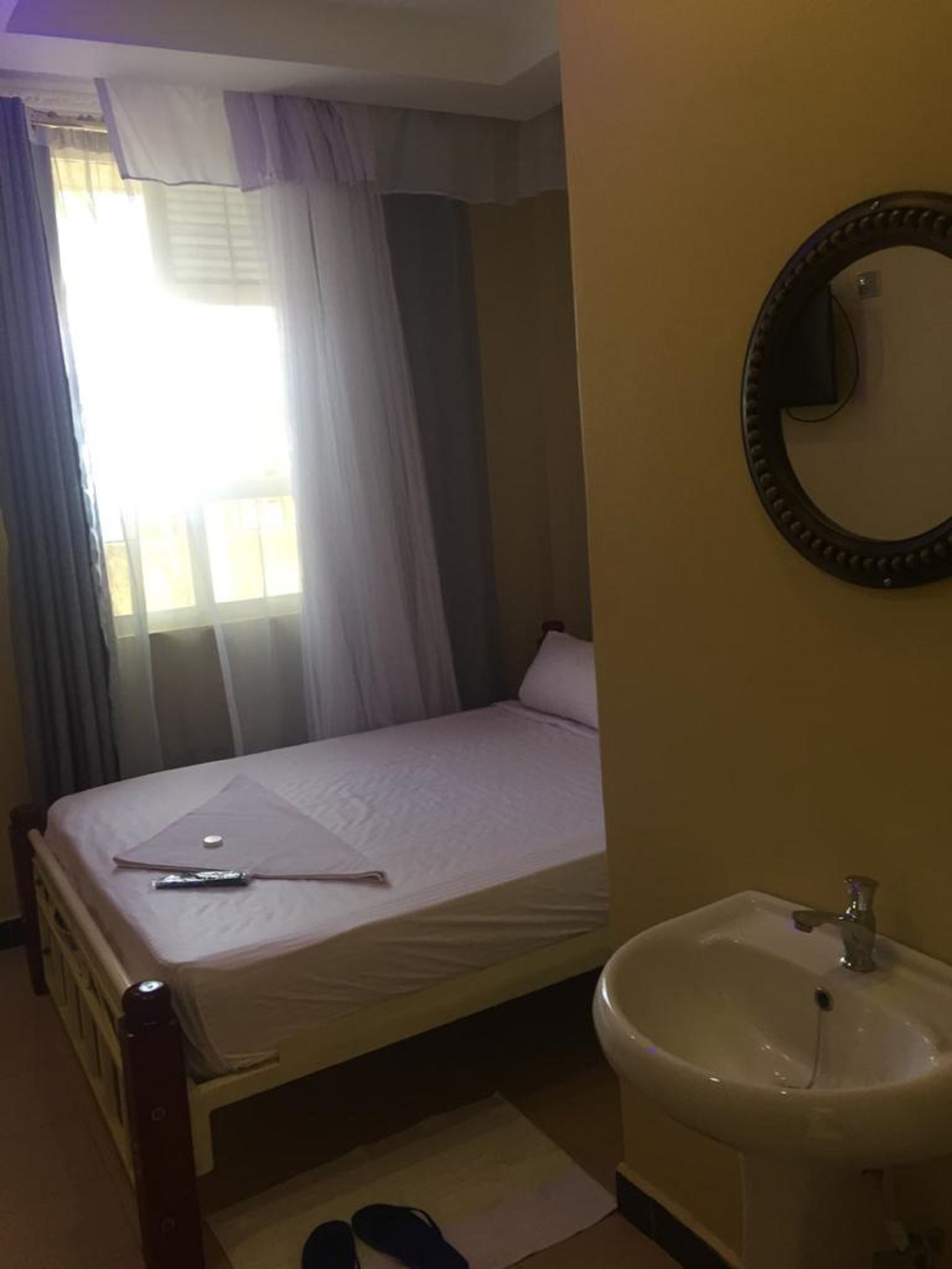 Una habitación de hotel con una cama, una mesita de noche, un espejo y un lavabo.