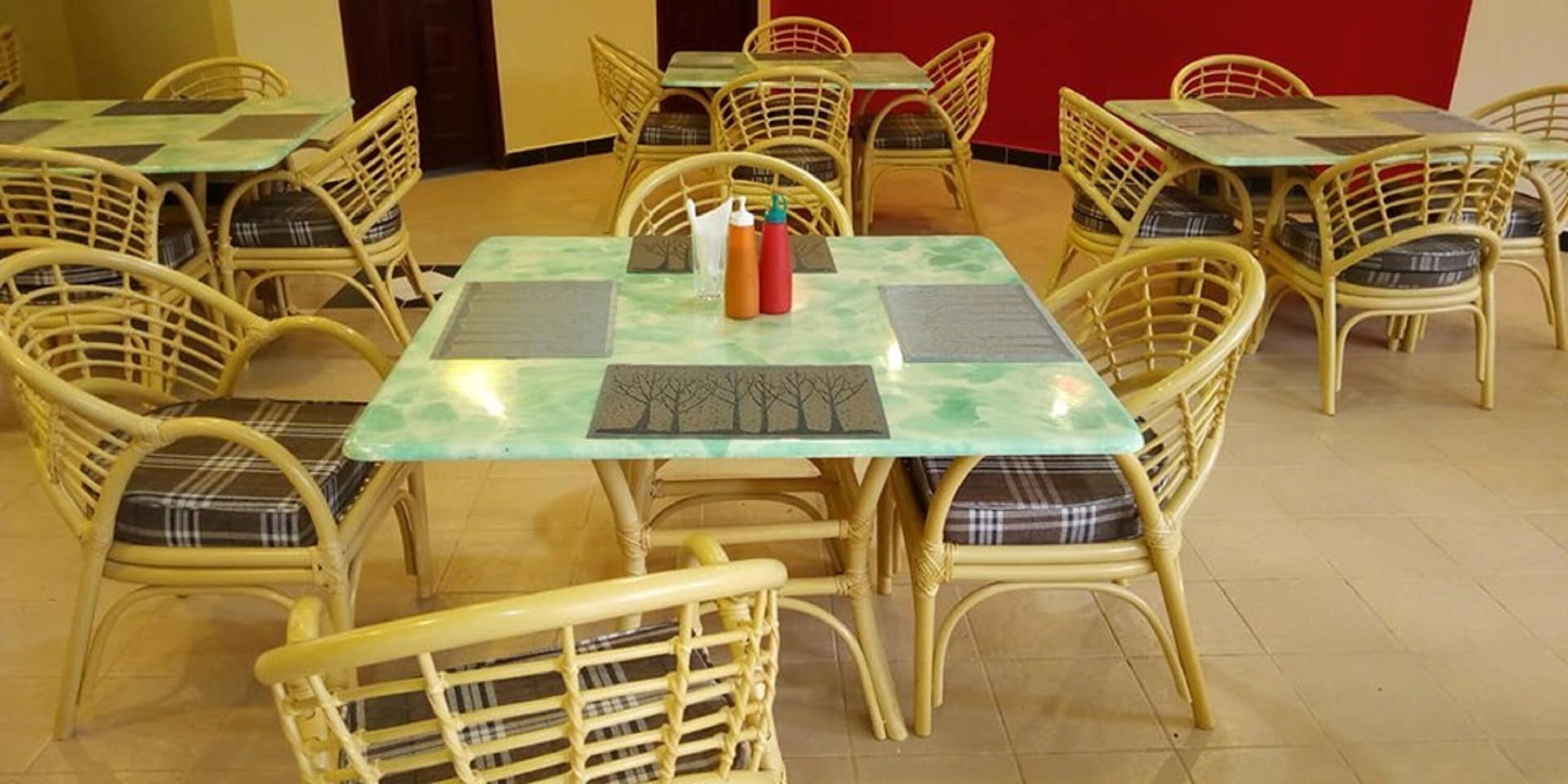 Un comedor con sillas y mesas de mimbre, algunas con manteles individuales y condimentos.
