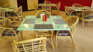 Un comedor con sillas y mesas de mimbre, algunas con manteles individuales y condimentos.