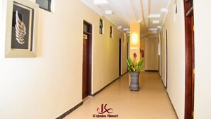 Un pasillo de hotel con diseño moderno, que presenta una lámpara central, obras de arte enmarcadas y una planta en maceta.
