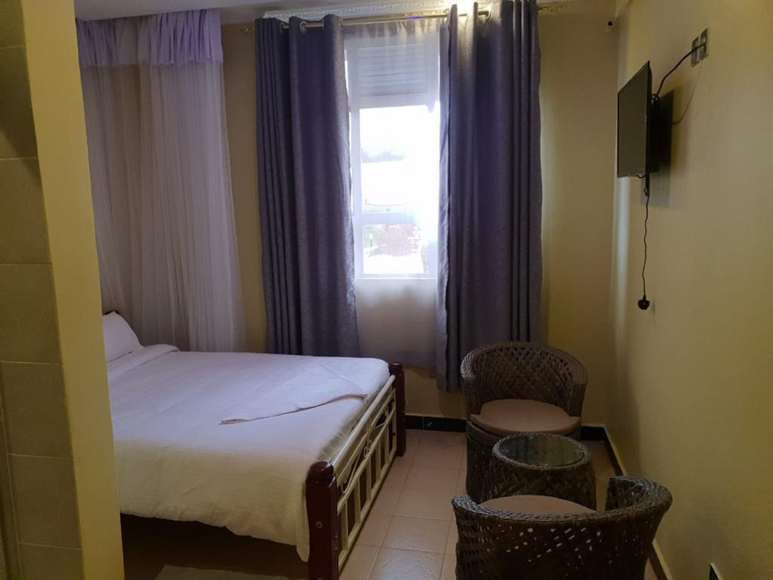A bedroom with a bed, a chair, a small table, and a TV on the wall.
