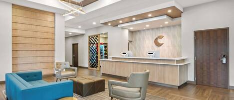A modern reception area with a wooden panel wall, a reception desk, a blue sofa, and a grey armchair.