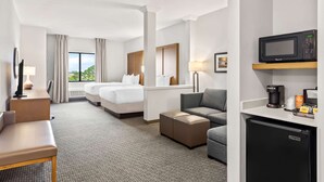 Una habitación de hotel con cama, sofá, escritorio, microondas, cafetera y refrigerador.