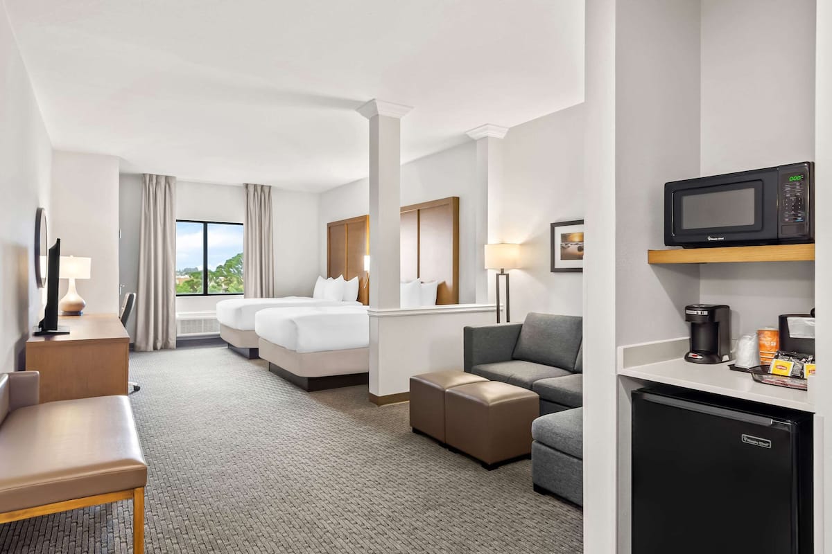 Una habitación de hotel con cama, sofá, escritorio, microondas, cafetera y refrigerador.