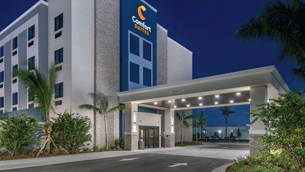 Un hotel Comfort Suites con diseño moderno, que cuenta con una entrada destacada con galería techada y vista despejada al estacionamiento.
