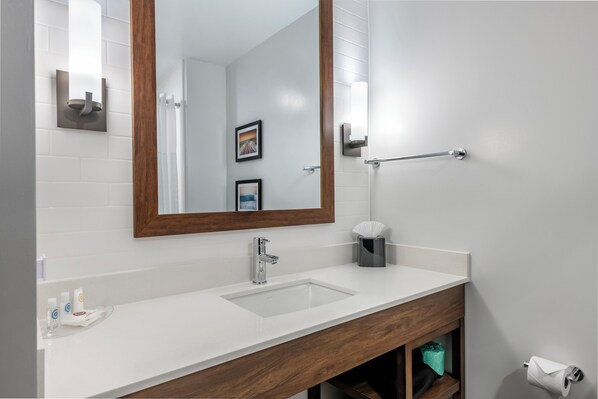 Un baño con lavamanos blanco, tocador de madera, un espejo grande y un perchero para toallas.