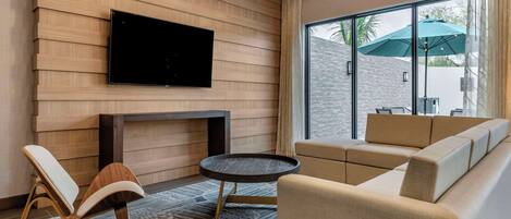 Una sala de estar moderna con un televisor de pantalla plana montado en una pared de madera, un sofá, un sillón y una pequeña mesa redonda.