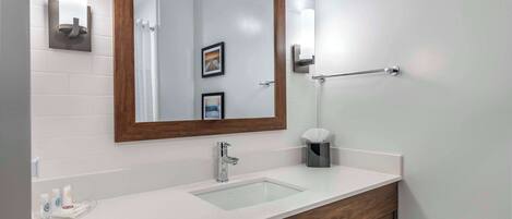 Un baño moderno con un lavabo blanco, tocador de madera y un espejo grande.