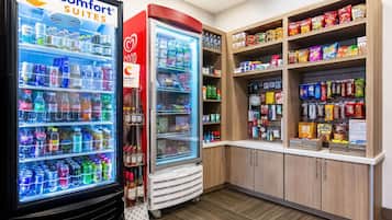 A hotel kitchenette with a refrigerator stocked with beverages, a freezer, and shelves of snacks and condiments.