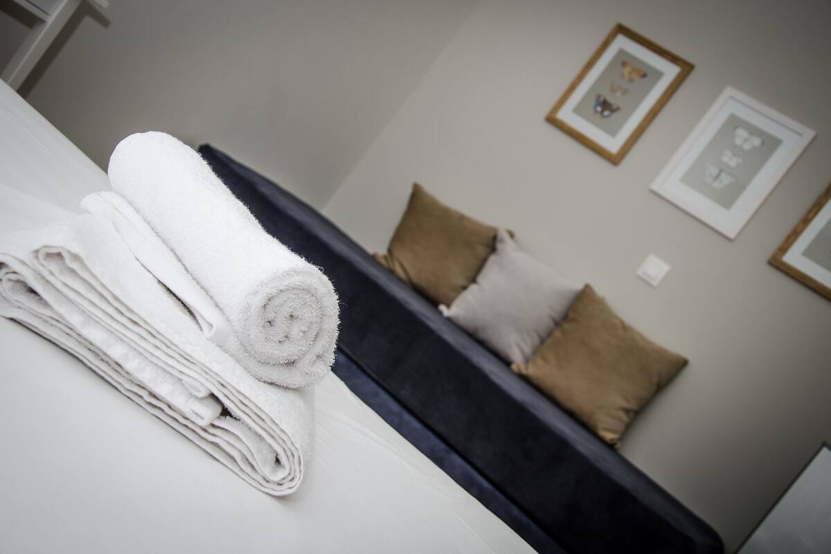 A neatly folded white towel on a bed in a hotel room with a dark headboard and beige pillows.