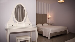 Een slaapkamer met een witte kaptafel, een ronde spiegel, een bed met hoofdbord en een bedlampje.
