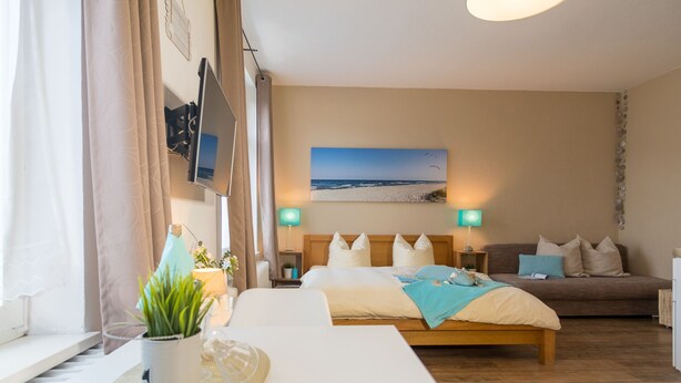 Une chambre à coucher avec un lit, des tables de chevet, une télévision, un tableau et une fenêtre avec des rideaux.