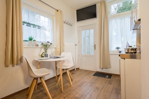 A compact kitchen with a dining area, a TV mounted above the door, and a window with curtains.