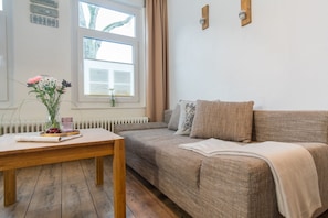 A cozy room with a wooden table, a sofa with a blanket, and a window with blinds.