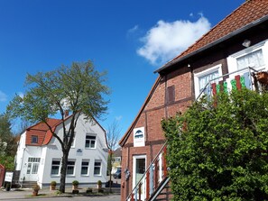 Ein traditionelles europäisches Gebäude mit rotem Ziegeldach, weißem Mauerwerk und einem Schild, das es als Mehrfamilienhaus kennzeichnet.