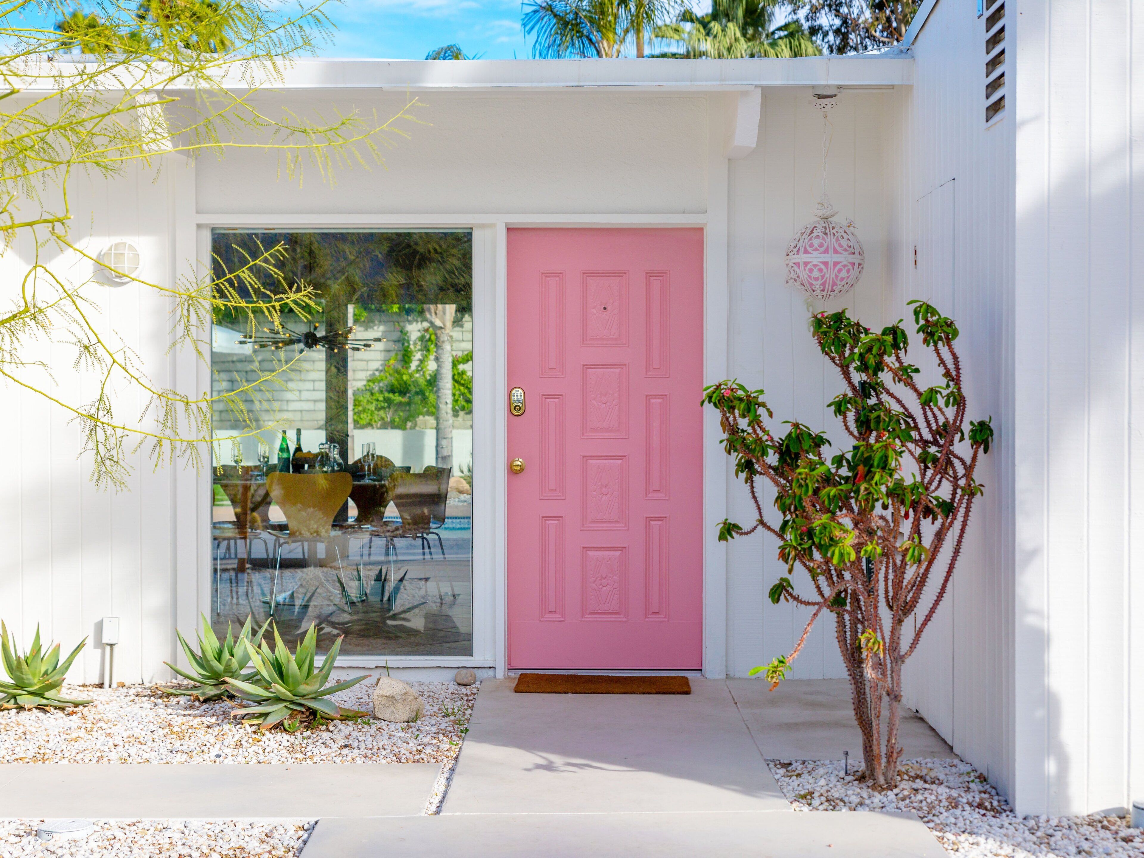 Une maison avec une porte rose, un petit jardin avec des plantes et une fenêtre en verre transparent.