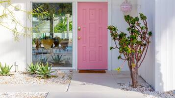 Une maison avec une porte rose, un petit jardin avec des plantes et une fenêtre en verre transparent.