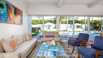 Un salon spacieux avec une table basse en verre, des sièges confortables, un grand tableau et une vue sur une piscine.