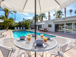 A poolside area with a round table, chairs, and umbrellas.