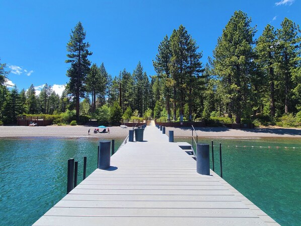 Un muelle de madera se adentra en un lago azul cristalino, rodeado de árboles verdes y frondosos.
