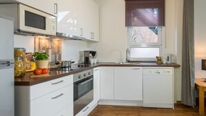 Eine moderne Küche mit weißen Schränken, einer Holz Arbeitsplatte, einem Einbauofen, einer Mikrowelle, einer Kaffeemaschine und einem Fenster mit Außenblick.