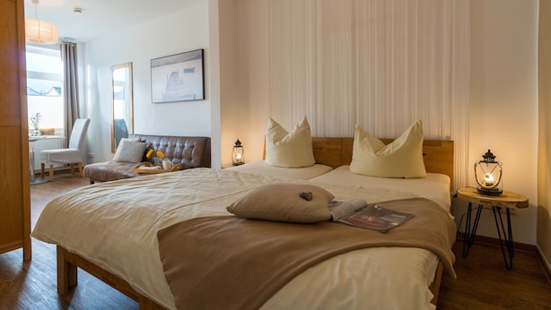 Ein Schlafzimmer mit einem großen Bett, zwei Nachttischen mit Laternen, einem Sessel, einem Schreibtisch und einem Fenster mit Vorhängen.
