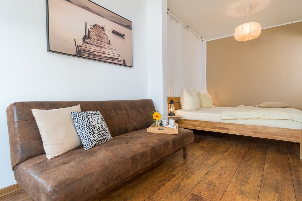 A modern room with a brown sofa, a wooden bed, a framed picture on the wall, and a hanging light fixture.