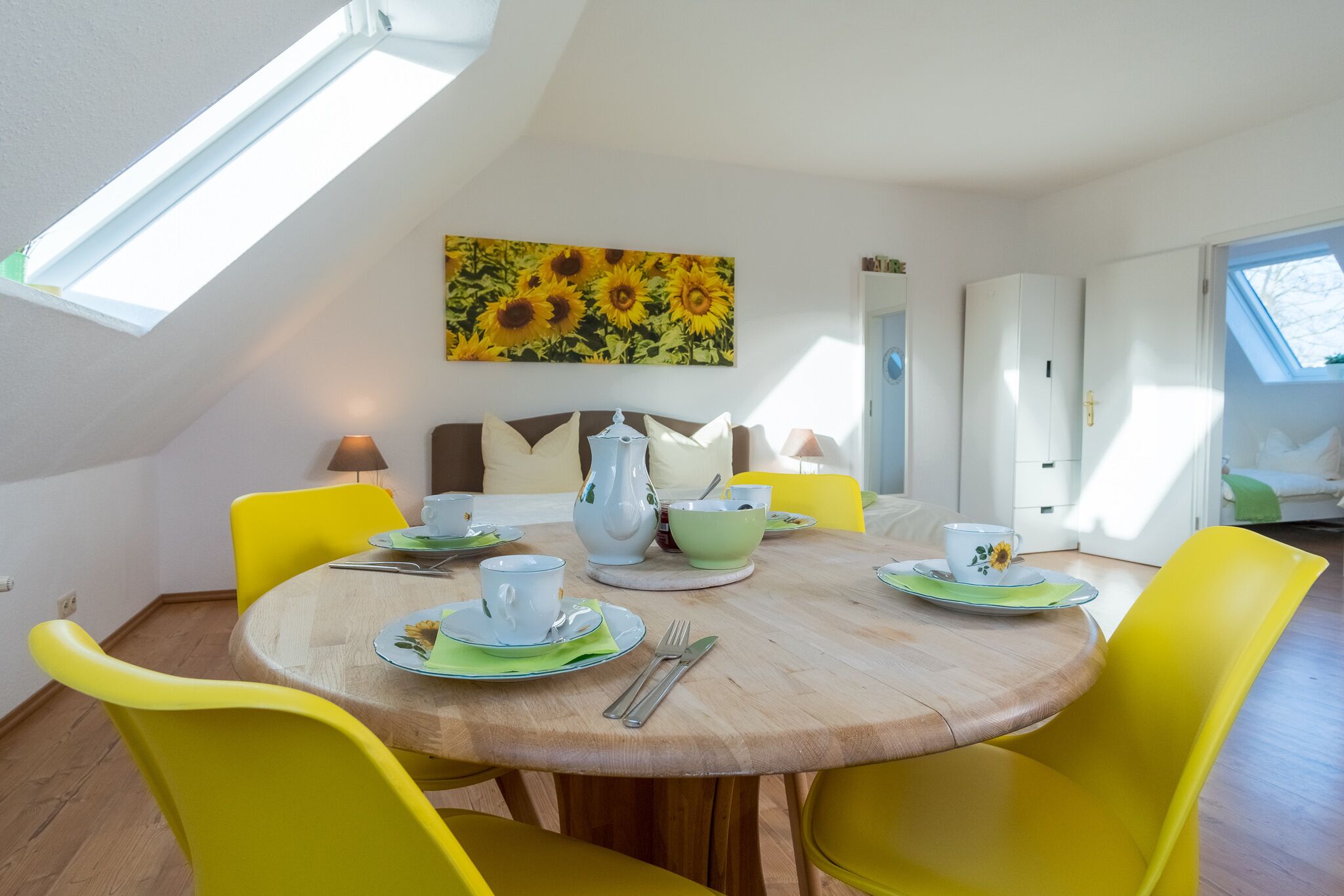 Un comedor con una mesa redonda de madera, sillas amarillas y un cuadro de un girasol en la pared.