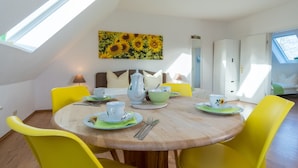 Ein Essbereich mit einem runden Holztisch, gelben Stühlen und einem Gemälde einer Sonnenblume an der Wand.