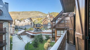 Un edificio de estilo chalé tradicional con un balcón de madera, un sendero adoquinado y una vista de una estación de esquí al fondo.