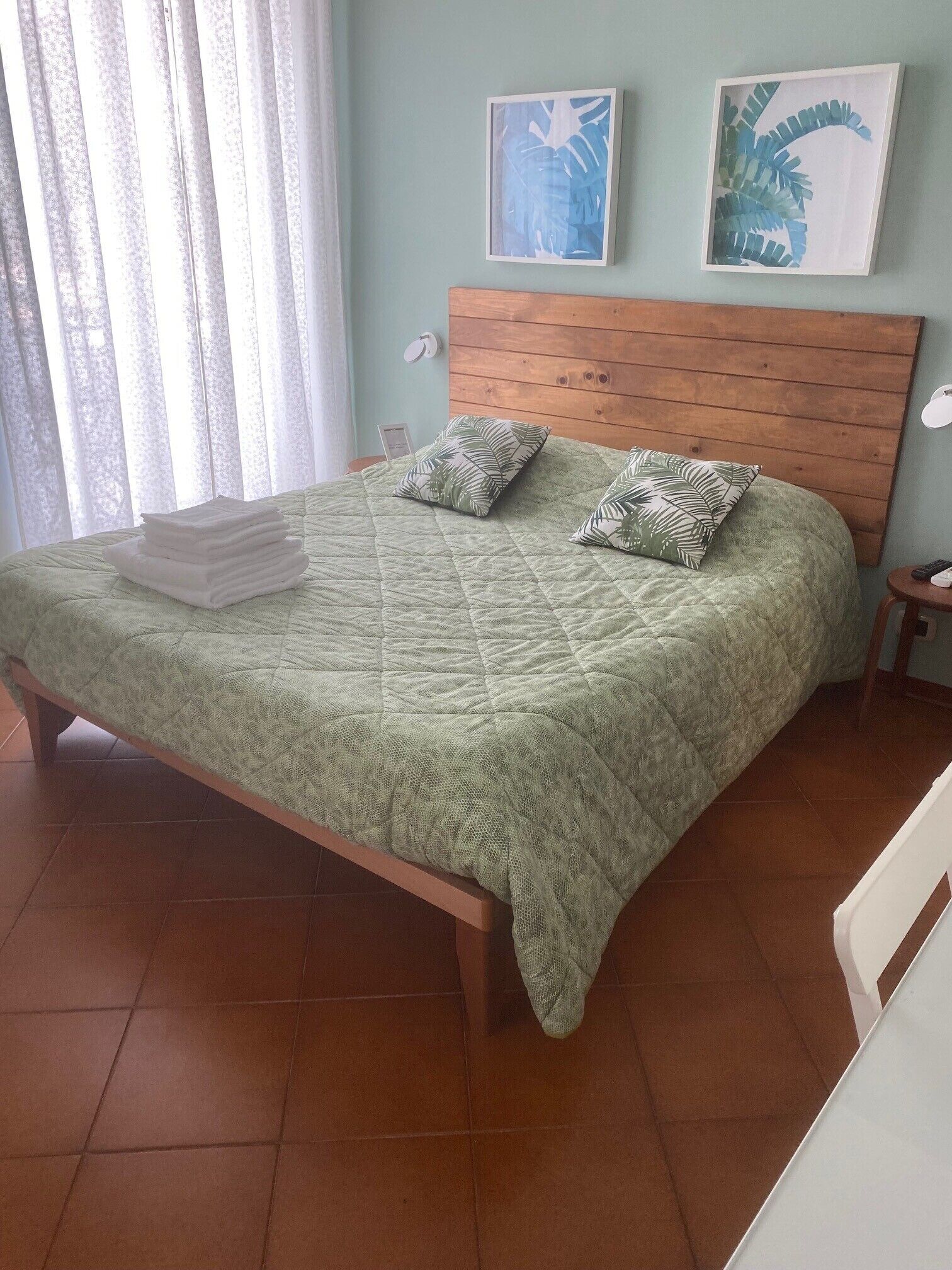 Un lit avec une couette verte, deux oreillers ornés de motifs de feuilles et une tête de lit en bois.
