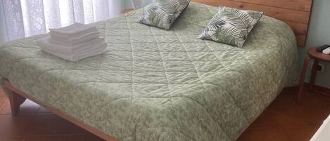 A bed with a green quilt, two pillows with leaf patterns, and a wooden headboard.