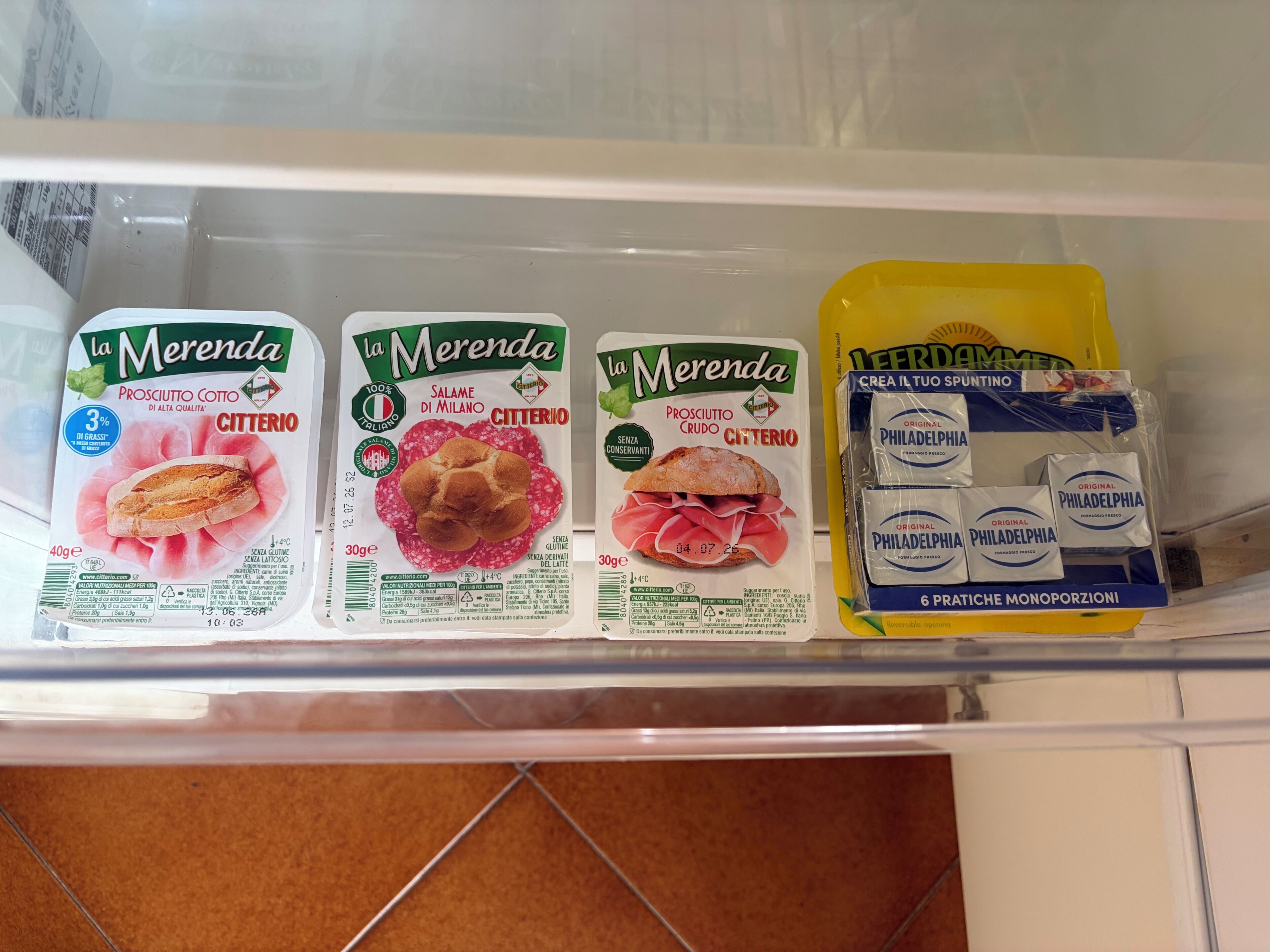 A refrigerator shelf with three packages of La Merenda salami and a box of Philadelphia cheese.
