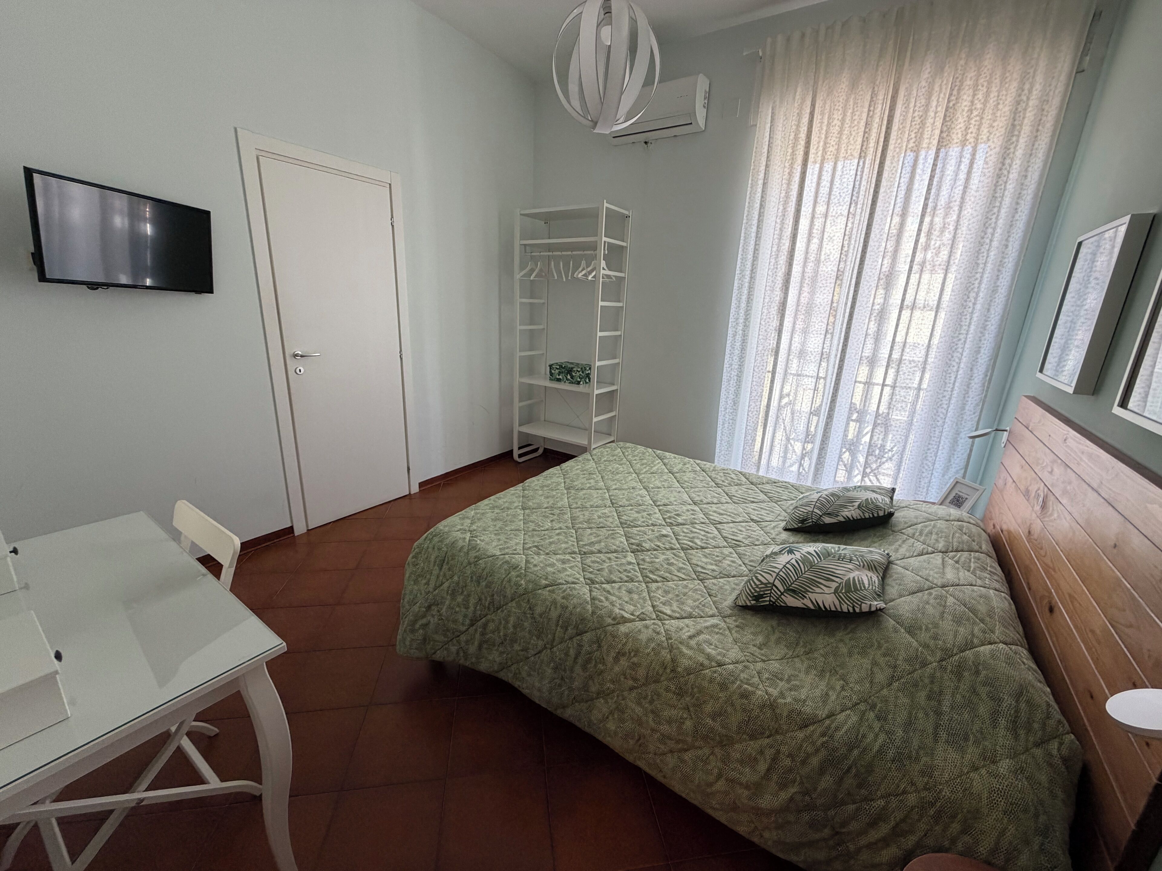 A bedroom with a bed, a TV, a wardrobe, and a window with curtains.