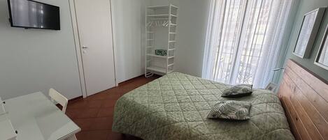 A bedroom with a bed, a TV, a wardrobe, and a window with curtains.