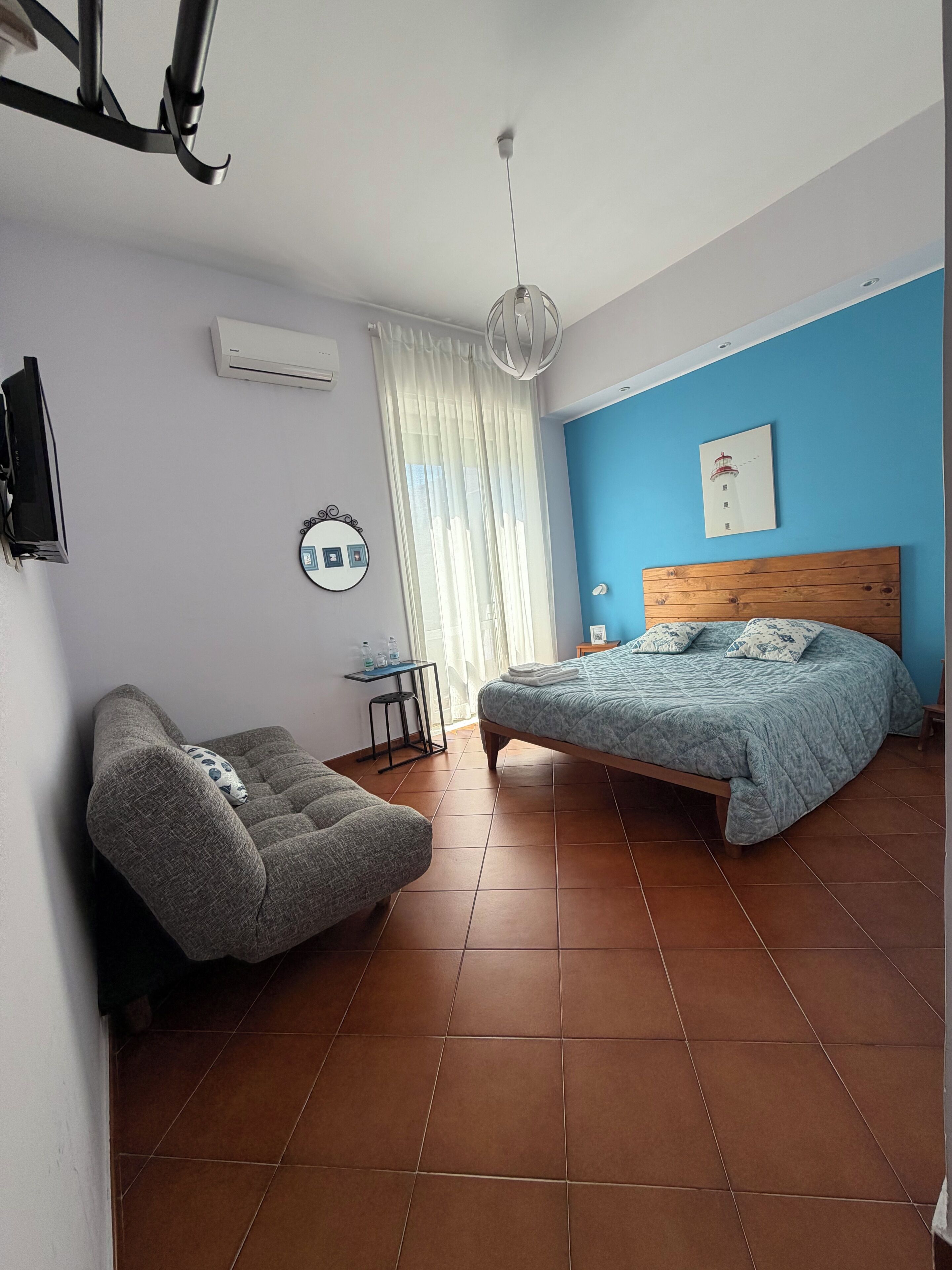 A bedroom with a bed, a chair, a desk, a hanging light fixture, and a wall-mounted air conditioner.