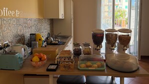A kitchen with a coffee & breakfast sign, a toaster, a kettle, a bowl of fruit, and various food items on the counter. - B&B Il Faro (Salerno)