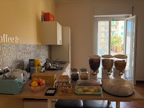 Et køkken med et skilt, der viser kaffe og morgenmad, en brødrister, en elkedel, en skål med frugt og diverse spiser på bordet.