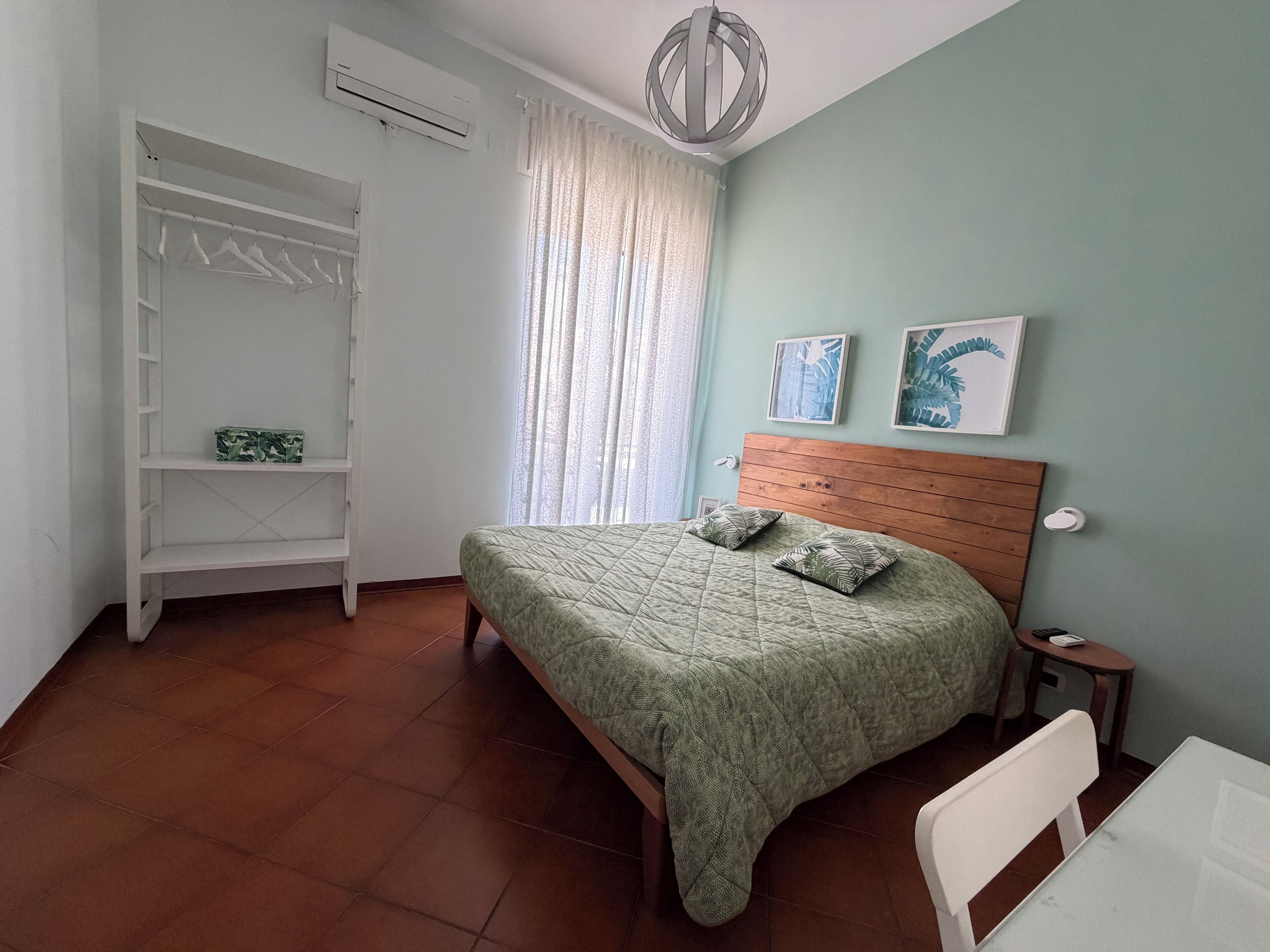 A bedroom with a bed, a wardrobe, a window with curtains, a bedside table, and a wall-mounted light fixture.