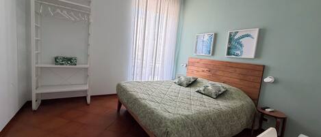 A bedroom with a bed, a wardrobe, a window with curtains, a bedside table, and a wall-mounted light fixture.
