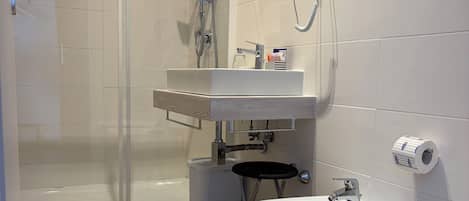 A bathroom with a glass shower enclosure, a sink with a mirror, two bidets, and a toilet.