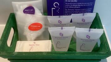 Un vassoio verde con un set da toeletta, un cofano doccia e diverse bottiglie di shampoo e sapone.