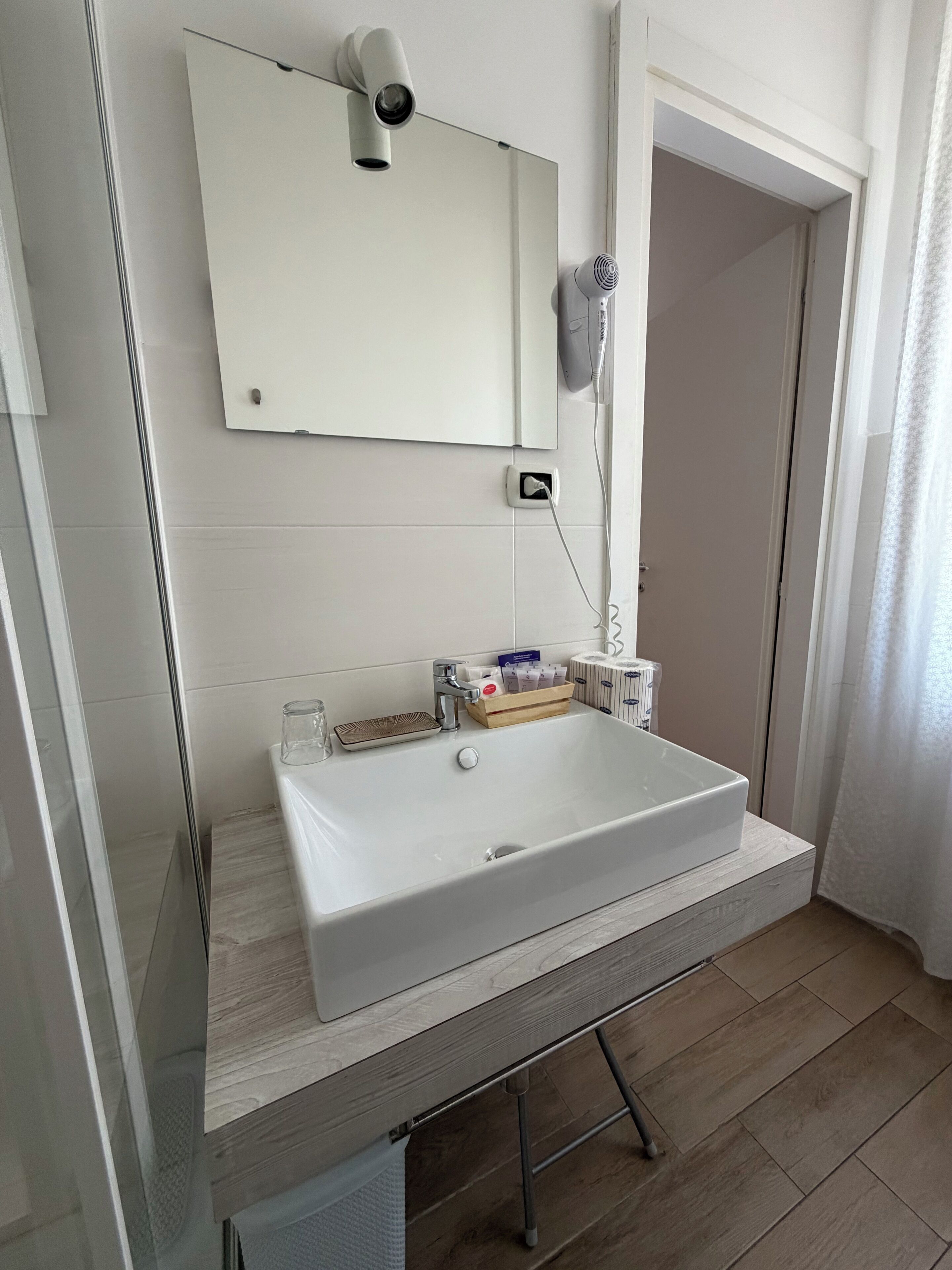 A bathroom with a white sink, a mirror, a hairdryer, and a glass shower enclosure.