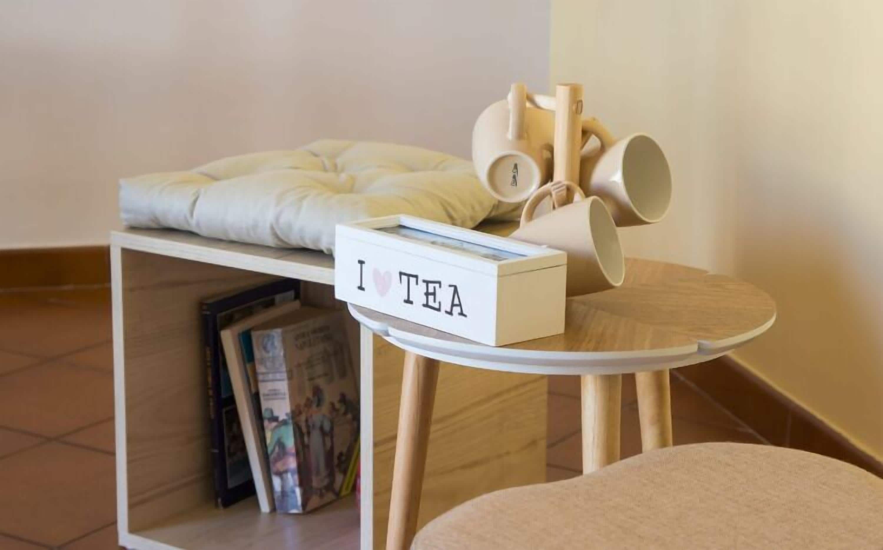 A small table with a 'I ♥ TEA' sign, a stack of teapots, and a cushion on a shelf.