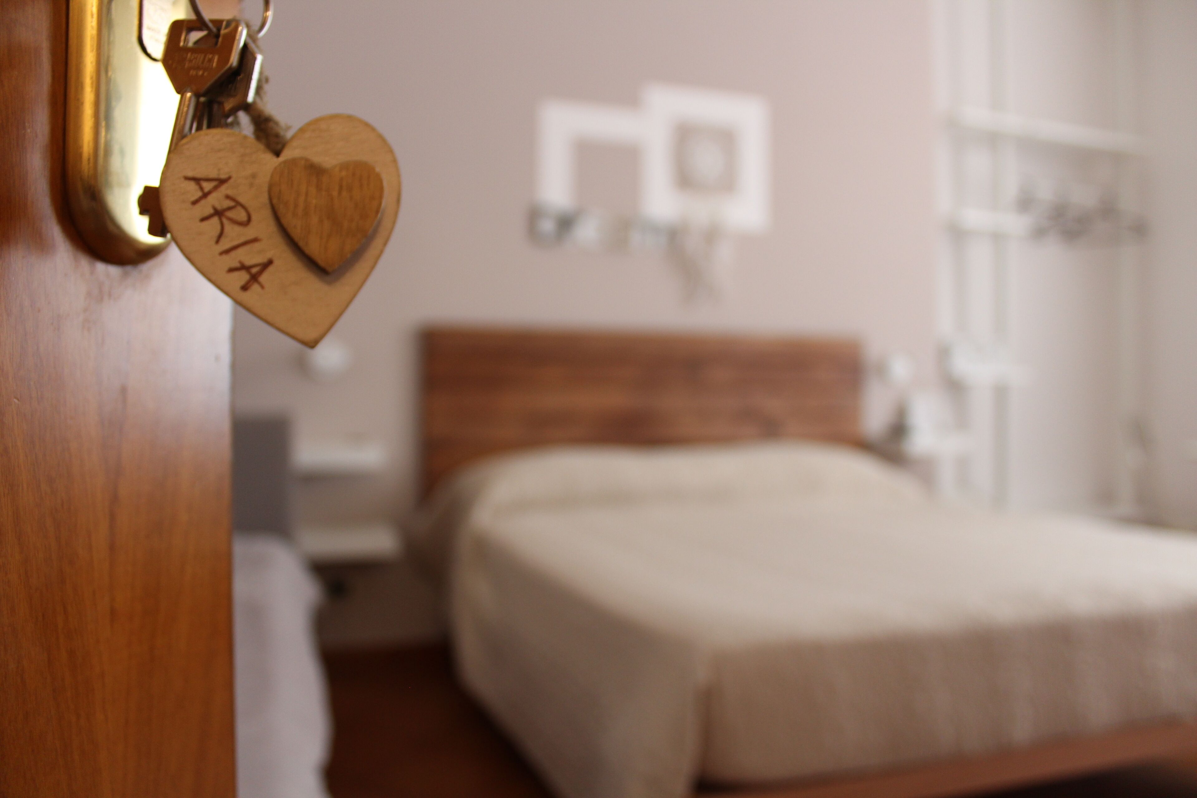 Une chambre avec une tête de lit en bois, un lit recouvert d’une couverture blanche et un porte-clés en forme de cœur accroché à la porte.