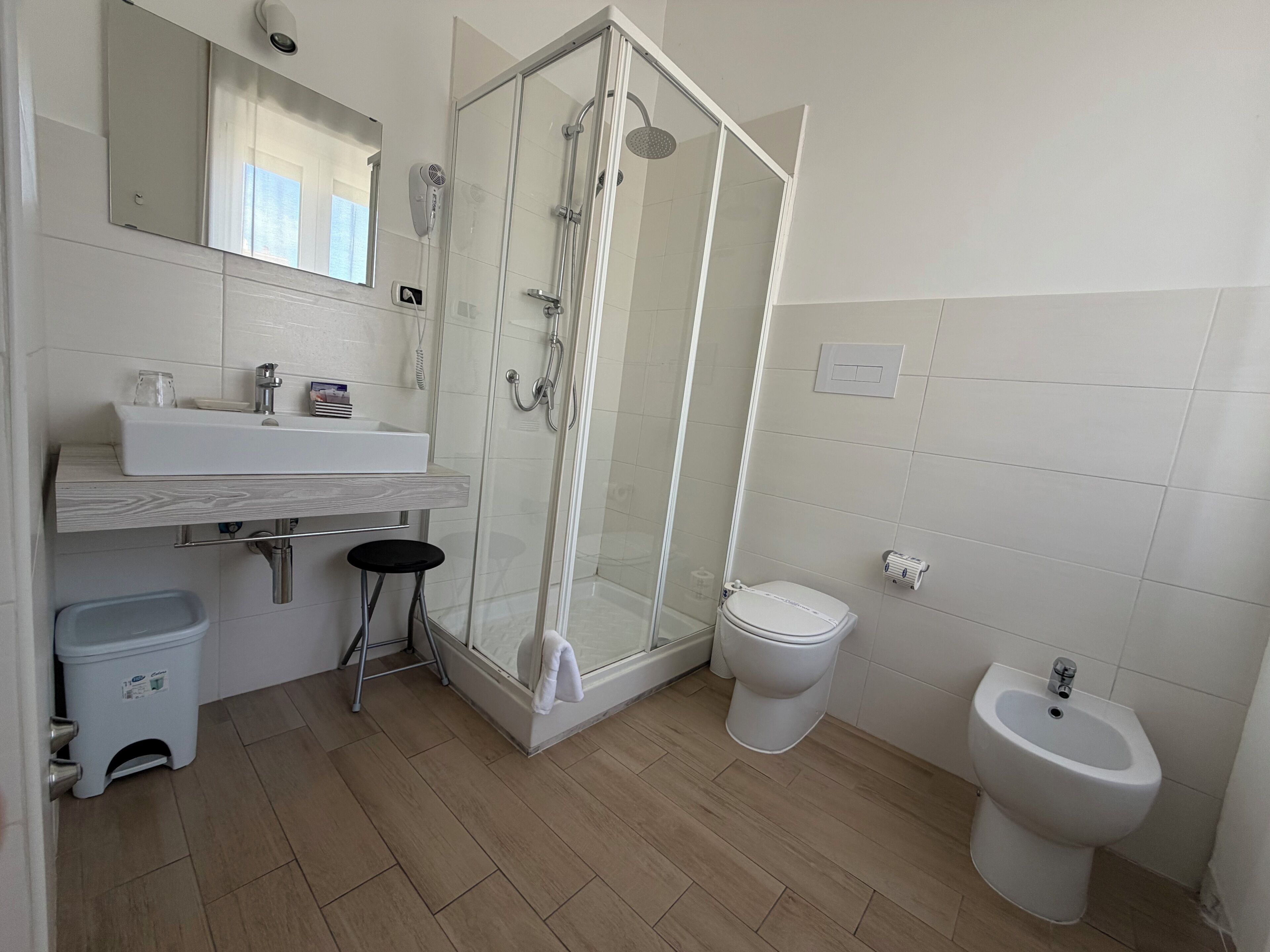 Une salle de bain avec une douche à parois de verre, des toilettes, un bidet, un lavabo et un miroir.