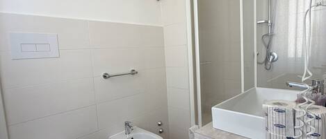 A bathroom with a toilet, bidet, bathtub, and a mirror with a showerhead.